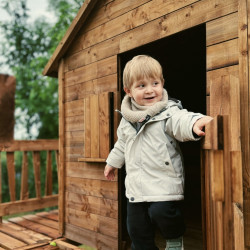 Enfant sortant d'une cabane en bois perchée ouvrant la porte avec un manteau souriant